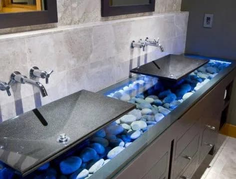 Custom dual vanity with a glass top over illuminated river stones